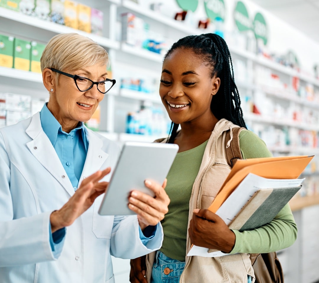 A pharmacist using digital tablet with young female customer in drugstore.